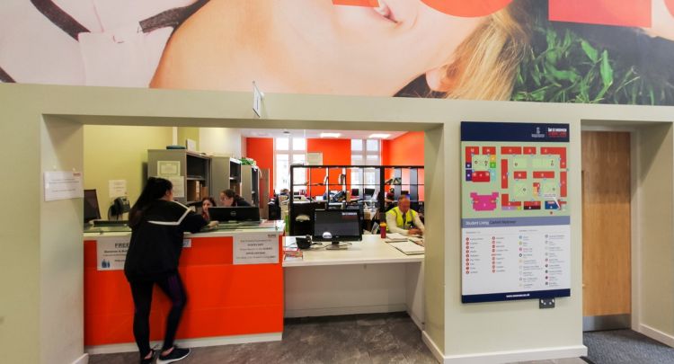 University reception desk with staff assisting at orange counter