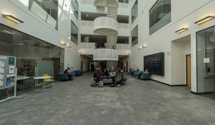 Bright atrium with glass roof, seating areas, posters, and office windows.