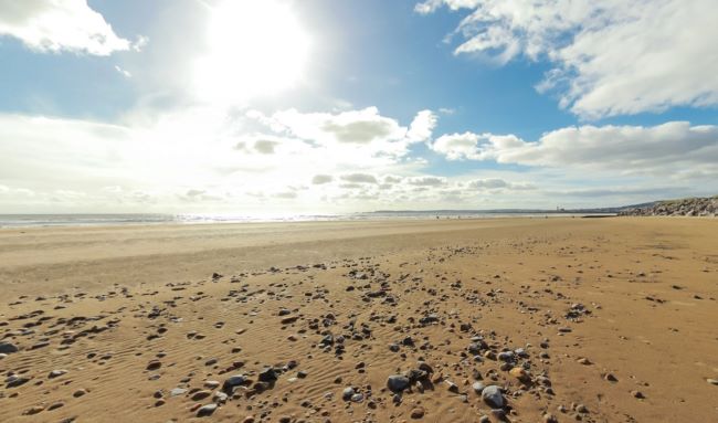 Wide sandy beach with scattered pebbles under a bright sky with clouds