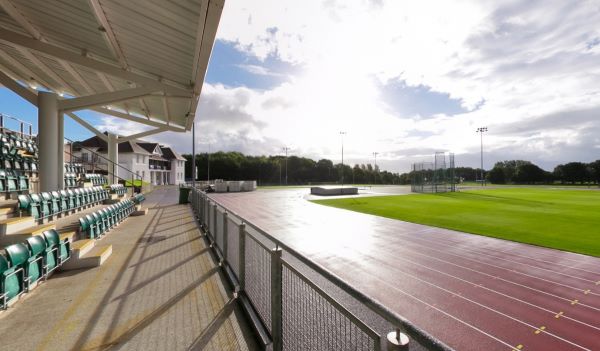 Outdoor athletics track beside covered seating and green sports field